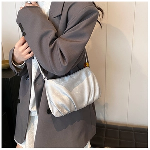 Detalle del bolso plisado plateado metálico con cuenta de ámbar sobre blazer gris
