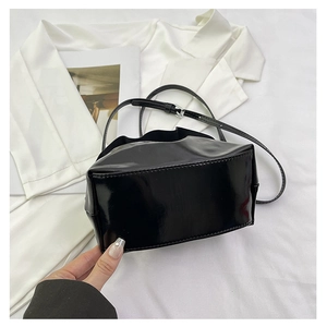 Detail view of black patent leather bucket bag with silver buckle and drawstring closure