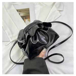 Detail of glossy black pleated cloud bag with metallic buckles and thin shoulder strap