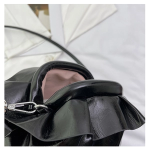 Detail of black glossy shoulder bag featuring wavy ruffles and pink fabric lining