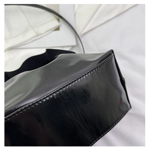 Detail view of the stitching and high-shine black glossy leather texture on the handbag