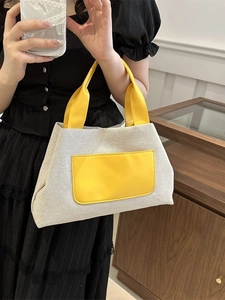 Chic cream canvas bucket bag with yellow leather handles shown in a lifestyle setting