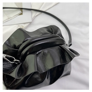 Detail of black glossy pleated clutch bag with cloud-like folds and silver hardware