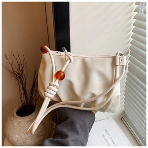 Detalle de bolso nube beige plisado con correas de nudo y cuentas de color ámbar