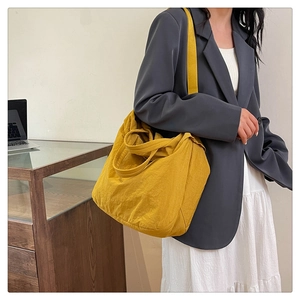 Grand sac cabas jaune en tissu texturé porté à l'épaule avec un ordinateur en arrière-plan