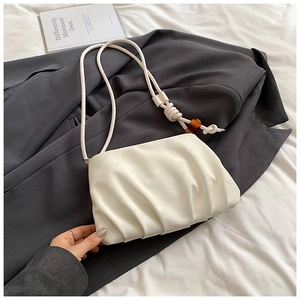 Detalle del bolso de nube plisado blanco con nudo elegante y cuenta de ámbar en la correa