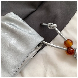 Detalle de bolso nube plisado plateado con correa de cuentas ámbar y acabado metálico