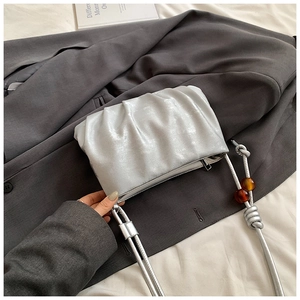 Detalle de bolso nube plateado con correa anudada y cuentas decorativas de ámbar