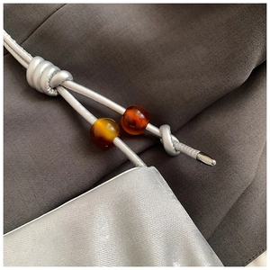 Detalle del bolso nube plisado plateado con asa de cuerda y cuentas de ámbar de lujo