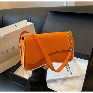 Detail van de oranje onderarmtas met witte randen en gouden ketting op een doos