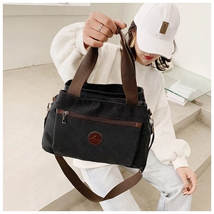 Dettaglio borsa a tracolla in tela con cinturini marroni, tasca zip e logo in pelle