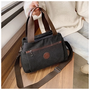 Dettaglio della borsa tote in tela nera con manici marroni e toppa con logo in pelle