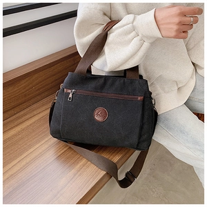 Dettaglio della borsa in tela nera con logo in pelle su legno, mostrando la trama del tessuto