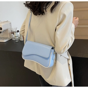 Detail van lichtblauwe crossbodytas met gegolfde flap en witte biezen in een café