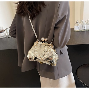 Detail of shell-shaped gold sequin bag with pearl strap worn over grey blazer