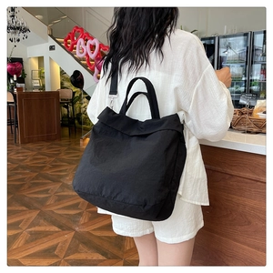 Détail du grand sac cabas noir porté par un mannequin dans un décor de café cosy