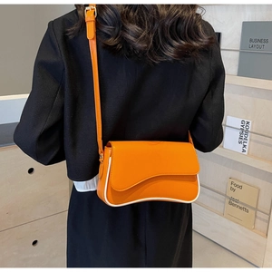 Felgekleurde oranje crossbodytas met witte contrastbiezen gedragen op een zwart jasje