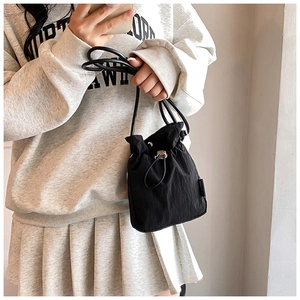 Detail view of black nylon drawstring bucket bag with adjustable shoulder strap and woven tag