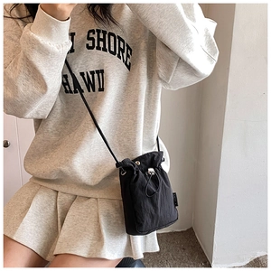 Detail view of black drawstring bucket bag worn over a gray sweatshirt and pleated skirt