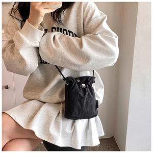 Detail of black nylon drawstring crossbody bag with side label and thin strap