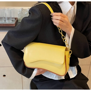 Detail van gele baguette tas met gebogen klep en gouden ketting bij het model