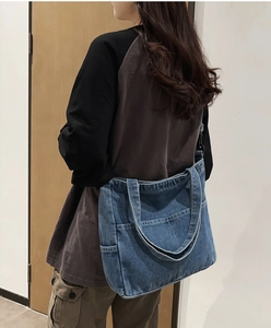Dettaglio della grande borsa tote in denim blu slavato con tasche e tracolla lunga