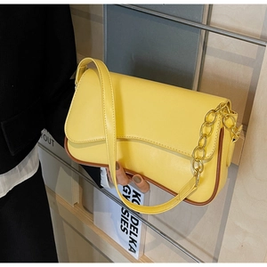 Detail van gele flap tas met getextureerd leer, bruine randen en gouden metalen ketting