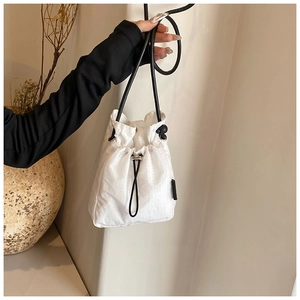 Detailed view of white drawstring bucket bag featuring square grid texture and black strap
