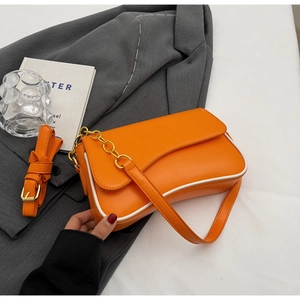 Detail van helder oranje crossbody tas met witte biezen en gouden ketting accenten