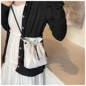 Detail of white checkered drawstring crossbody bag featuring silver snap button and black strap