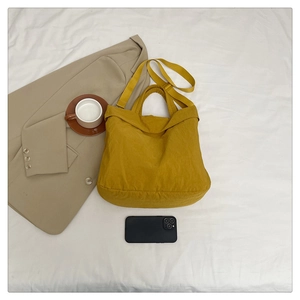 Détail d'un sac cabas en nylon jaune gingembre avec doubles sangles sur un lit épuré