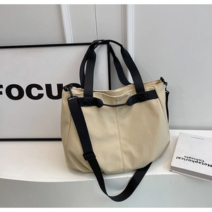 Detail of a large cream canvas tote bag with black contrast straps and detachable shoulder strap