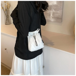Detail of white nylon drawstring bucket bag with textured grid fabric and black shoulder strap