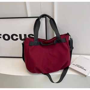 Close-up of burgundy canvas tote bag featuring black nylon straps and matte hardware
