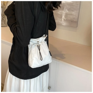 Modern white quilted drawstring bucket bag with adjustable black strap worn by a model
