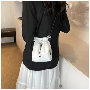 Rear view of a white nylon drawstring crossbody bag worn with a black casual top