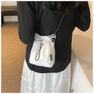 Detail of white nylon drawstring crossbody bag with black VEILA logo and adjustable strap