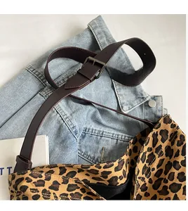 Detail of adjustable dark brown leather strap with metal buckle on leopard print canvas tote