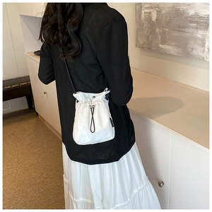 Rear view of model wearing a white nylon mini drawstring bucket bag with black strap