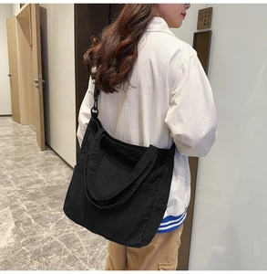 Vista laterale della grande borsa tote in tela nera indossata da una modella in interni