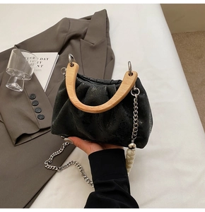 Détail du sac plissé en cuir gris avec poignée en bois en U et chaîne en perles blanches