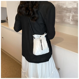 Close-up of white nylon drawstring crossbody bucket bag with black strap and quilted texture