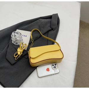 Detail van gele baguette tas met bruine rand en gouden ketting op een grijze blazer