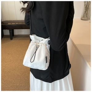 Detail of white nylon drawstring bucket bag with subtle grid texture and black strap