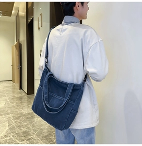 Dettaglio di una borsa tote in denim blu scuro con tracolla nera regolabile sulla modella