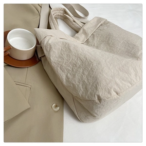 Détail d'un sac cabas beige en tissu plissé associé à un élégant blazer kaki