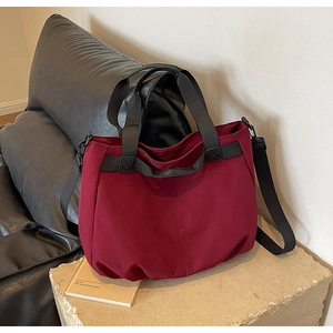 Close-up of deep burgundy canvas tote bag with black woven handles on a stone pedestal