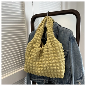 Detail of light yellow bubble texture tote bag hanging on wooden hanger with denim background