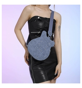 Detail of blue denim guitar-shaped crossbody bag with silver studs and nylon strap