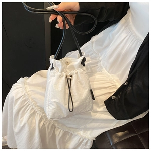 Detail of white mini drawstring bucket bag showing its textured fabric and metal snap closure